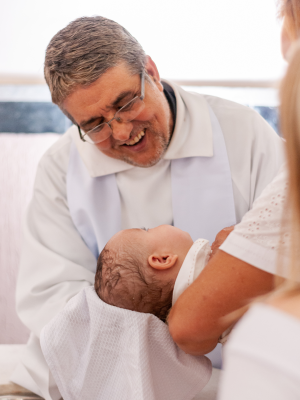 Priester lächelt bei der Taufe eines Babys im Arm der Mutter